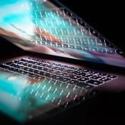 half-open laptop with pink and blue lights in a dark room